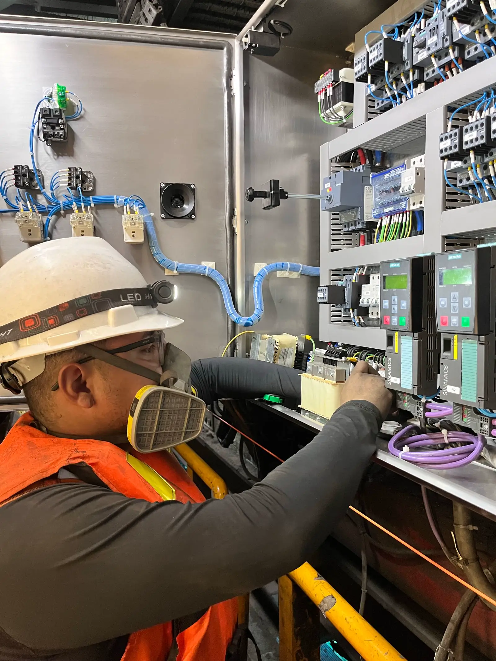 Técnico con casco blanco, respirador y antiparras trabajando en un tablero eléctrico
