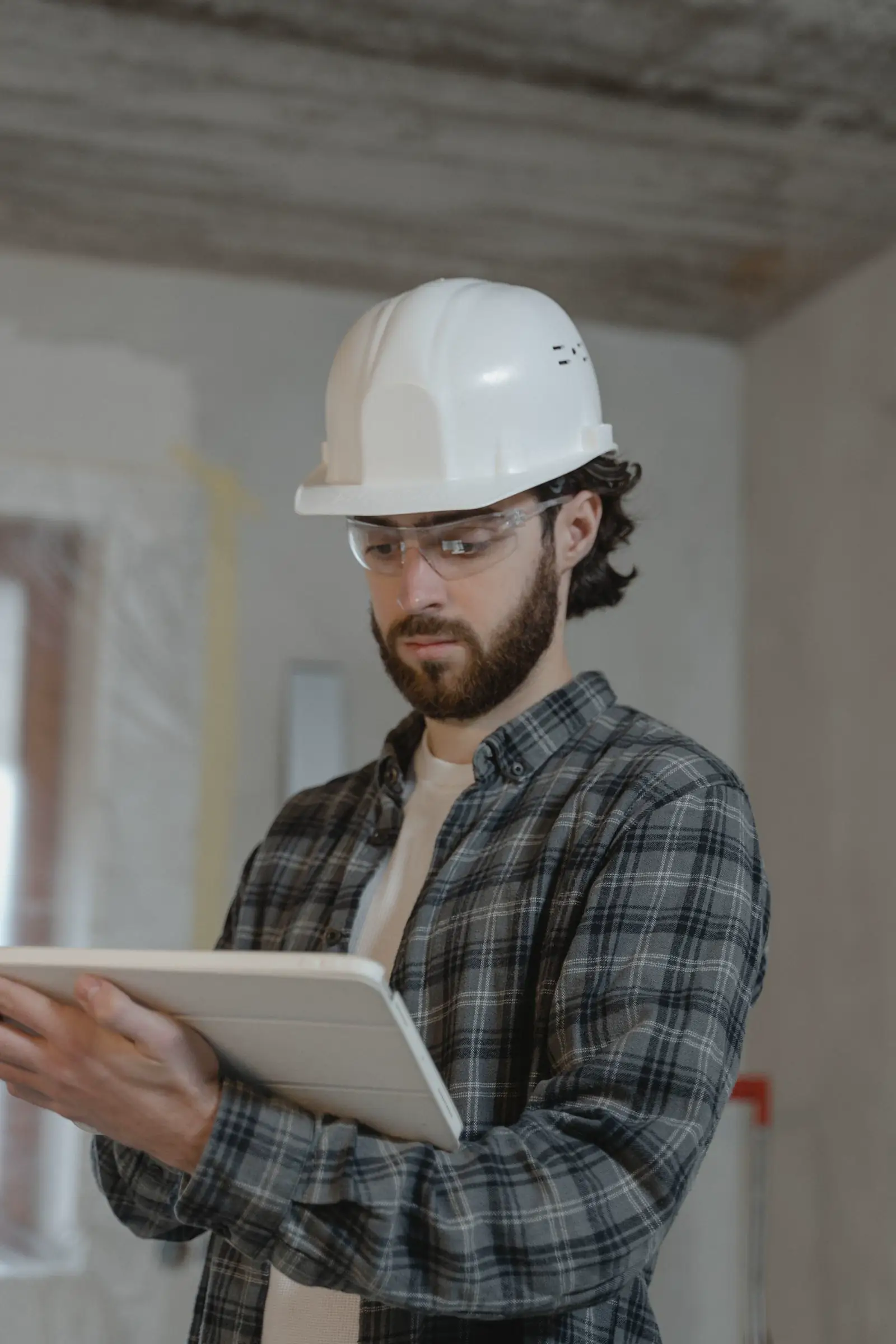 Profesional con casco blanco y tablet inspeccionando una obra